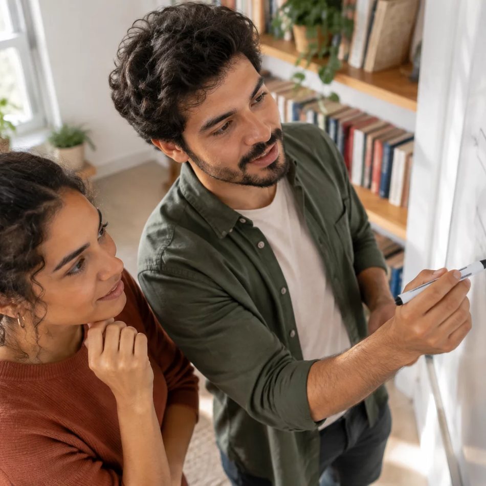Duas alunas sentadas de frente uma para a outra numa mesa da sala em Cuiabá; a da direita anota a resposta que vai dar
